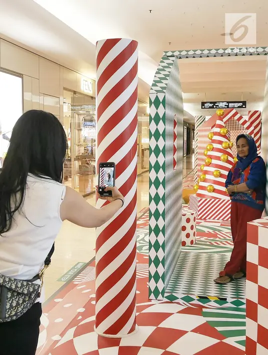 Pengunjung berfoto di depan pohon Natal yang menghiasi pusat perbelanjaan di kawasan Menteng, Jakarta, Minggu (23/12). Konsep dekorasi pohon Natal modern disajikan untuk membuat suasana berbeda dari tahun-tahun sebelumnya. (Liputan6.com/Herman Zakharia)
