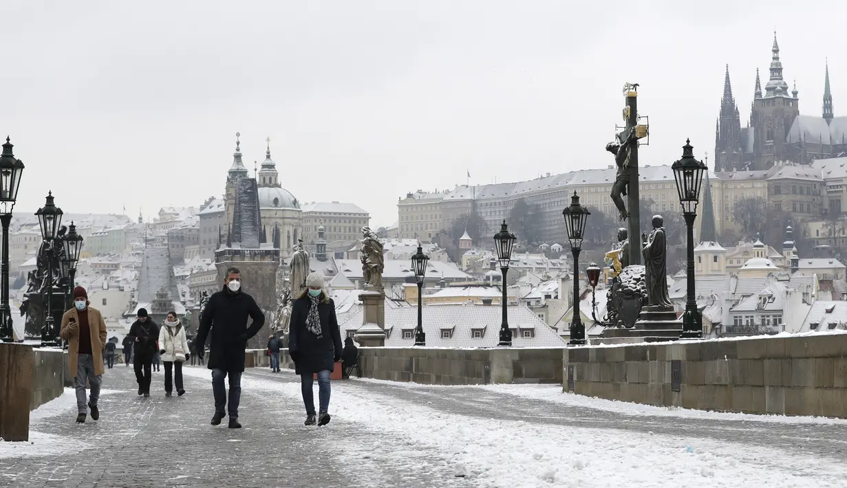Orang-orang menyeberangi Jembatan Charles abad pertengahan setelah hujan salju pertama di Praha, Republik Ceko (3/12/2020). (AP Photo / Petr David Josek)