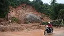 Pengendara motor melihat sebuah batu besar usai tanah longsor di Paung, negara bagian Mon (9/8/2019). Tanah longsor yang disebabkan oleh hujan lebat menewaskan sedikitnya 13 orang dan melukai puluhan lainnya di Myanmar timur. (AFP Photo/Ye Aung Thu)