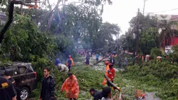 Warga membersihkan dahan pohon tumbang yang menimpa mobil di Kota Tangerang, Banten, Kamis (23/12/2021). Puluhan pohon dan gapura tumbang akibat terjangan angin kencang saat hujan lebat melanda Kota Tangerang. (Liputan6.com/Angga Yuniar)
