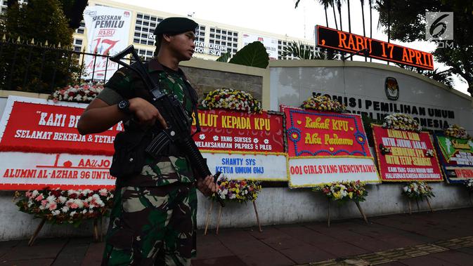 Tentara bersenjata  berjaga dekat karangan bunga yang ada di Gedung Komisi Pemilihan Umum (KPU), Jakarta, Sabtu (20/4). Karangan bunga terus berdatangan ke Gedung KPU. (merdeka.com/Imam Buhori)