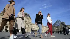 Turis tanpa mengenakan masker berjalan di sebelah Museum Louvre, di Paris, Senin (14/3/2022). Prancis telah mencabut sebagian besar pembatasan COVID-19 pada hari Senin, memungkinkan orang melepas masker di hampir semua tempat. (AP Photo/Francois Mori)