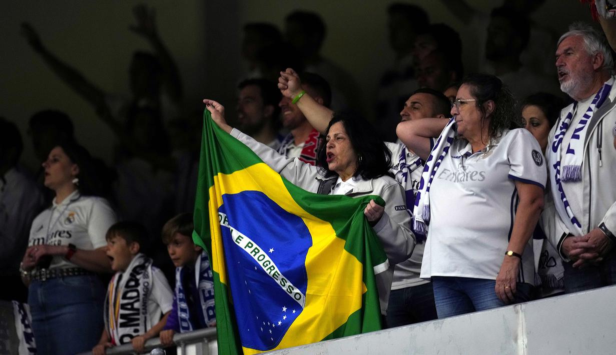 Pendukung Real Madrid membawa bendera Brasil pada laga lanjutan Liga Spanyol 2022/2023 antara Real Madrid melawan Rayo Vallecano pada Kamis (25/05/2023) dini hari WIB. Los Blancos memberikan aksi solidaritas sebelum laga tersebut setelah Vinicius Jr menjadi korban rasisme pada Minggu (21/05/2023) lalu. (AP Photo/Manu Fernandez)