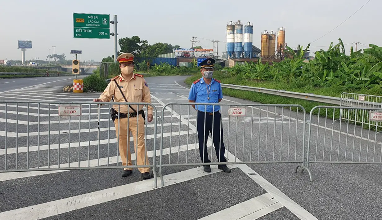 Polisi berjaga di belakang barikade yang didirikan untuk mengatur lalu lintas di Hanoi, Sabtu (24/7/2021). Vietnam memberlakukan penguncian wilayah (lockdown) selama 15 hari di ibu kota Hanoi mulai Sabtu ketika gelombang virus corona menyebar dari wilayah Delta Mekong selatan. (AP Photo/Hieu Dinh)