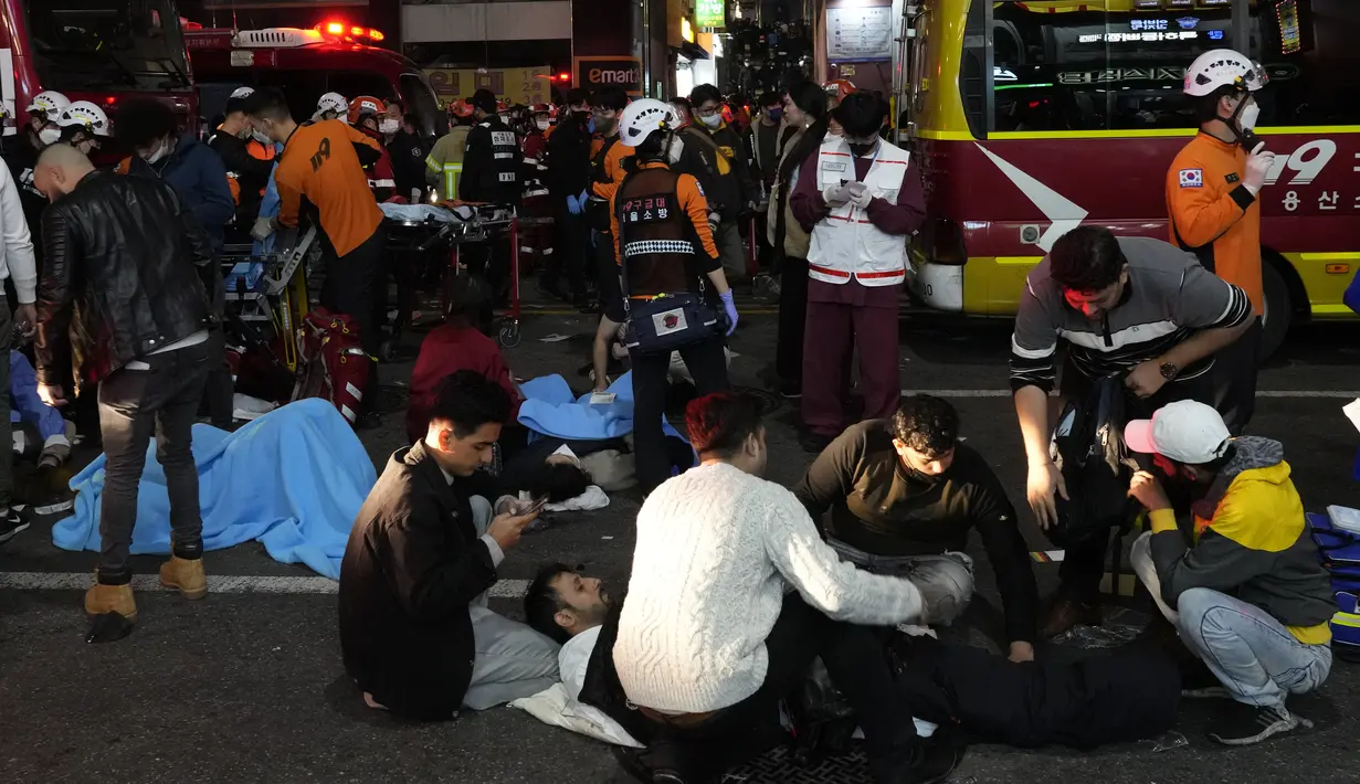 Petugas penyelamat dan petugas pemadam kebakaran berusaha membantu orang-orang yang terluka di dekat lokasi kerumunan massa di Seoul, Korea Selatan, Minggu (30/10/2022).  Pihak berwenang mengatakan mereka sedang menyelidiki penyebab pasti insiden perayaan Halloween Itaewon tersebut. (AP Photo/Ahn Young-joon)