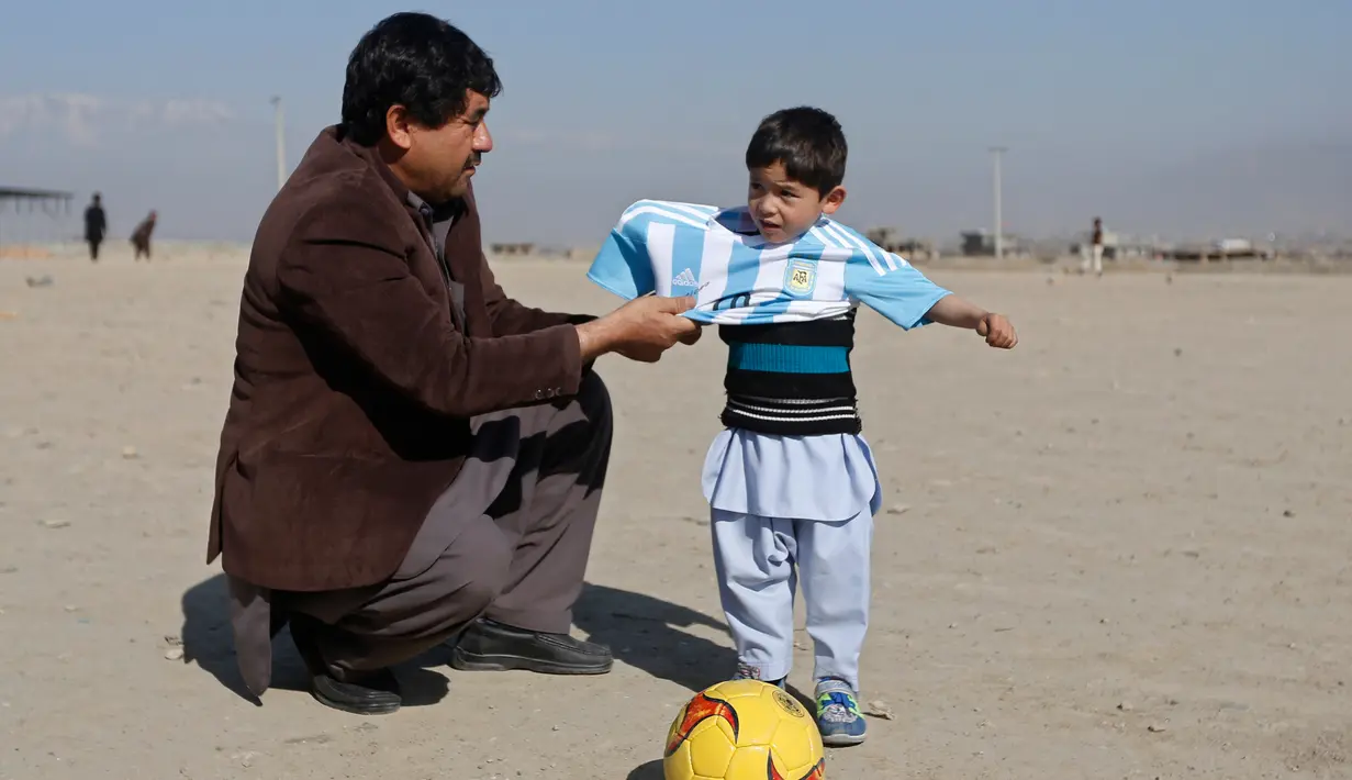 Murtaza Ahmadi (5), bocah asal Afghanistan, dibantu ayahnya memakai jersey yang ditandatangani langsung oleh bintang Barcelona, Lionel Messi, ketika bersiap main sepak bola di sebuah lapangan terbuka di Kabul, Jumat (26/2). (REUTERS/Omar Sobhani)