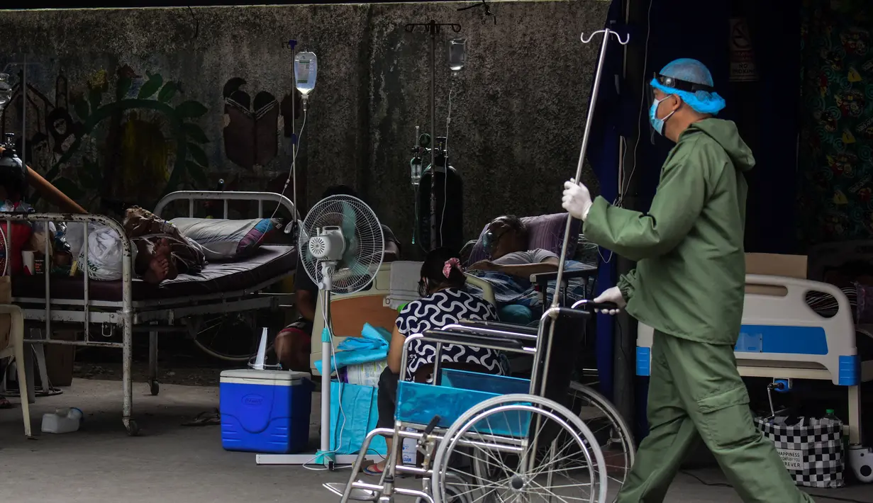 Seorang perawat berjalan melewati pasien terduga Covid-19 yang sedang beristirahat di tempat parkir yang diubah menjadi bangsal di luar rumah sakit di kota Binan, Manila, di tengah rekor infeksi yang dipicu oleh varian Delta yang sangat menular pada Senin (6/9/2021). (Photo by Maria Tan / AFP)