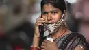 Seorang perempuan berbicara di telepon, maskernya diletakkan di dagu, di pusat vaksinasi di Hyderabad, India, 12 Januari 2022. Wajib pakai masker di India. Dan polisi turun ke jalan, mengawasi orang-orang untuk memastikan mereka ada di tempat.  (AP Photo/Mahesh Kumar A.)