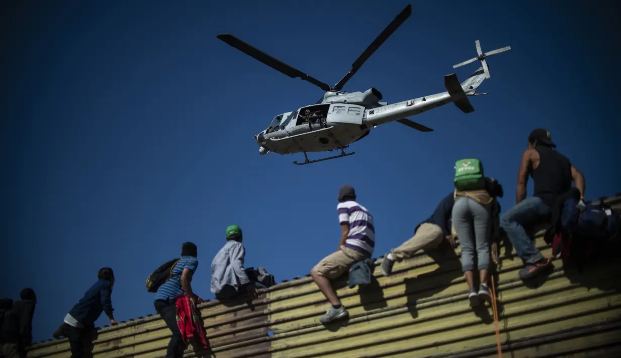 Sebuah helikopter terlihat saat para imigran memanjat pagar perbatasan antara Meksiko dan AS di Tijuana, Meksiko (25/11). Ratusan migran berusaha menyerbu pagar perbatasan yang memisahkan Meksiko dari AS. (AFP Photo/Pedro Pardo)