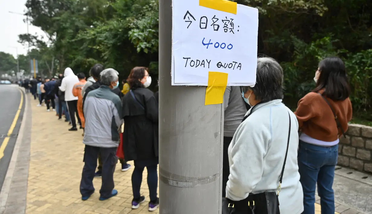 Orang-orang menunggu di sebelah tanda tentang nomor kuota harian ketika antrean panjang mengular di jalan untuk stasiun pengumpulan spesimen bergerak untuk pengujian Covid-19 di distrik Tung Chung, Hong Kong pada 10 Februari 2022. (Peter PARKS/AFP)