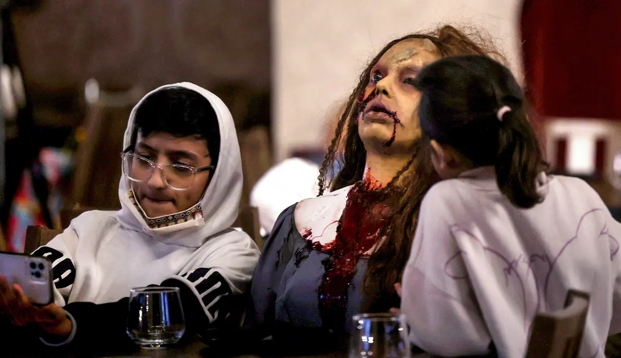 Seorang zombie duduk di meja dengan pengunjung di restoran "Shadows" bertema horor di kota hiburan Boulevard, Riyadh, Arab Saudi, 19 Januari 2022. Restoran tersebut menawarkan pengalaman unik kepada pelanggan dari hidangan dengan tengkorak dan darah ditemani zombie serta vampir (Fayez Nureldine/AFP)