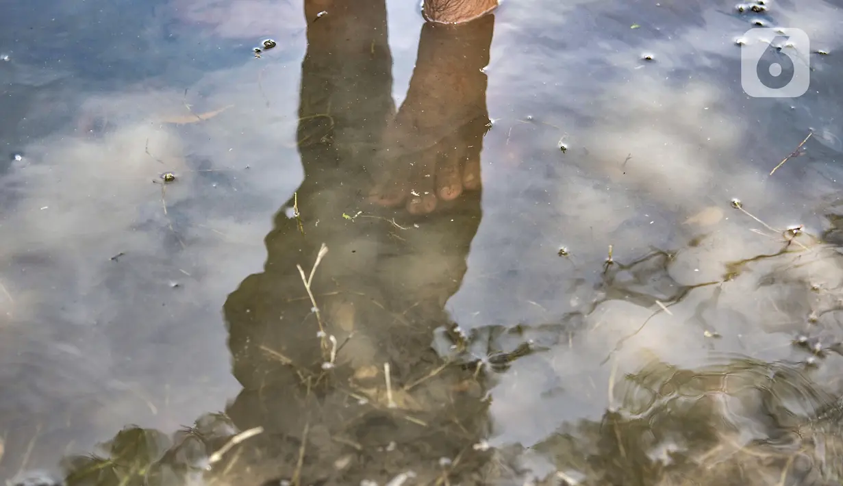 Refleksi bayangan Amir saat memancing di genangan air yang membanjiri TPU Semper, Jakarta, Selasa (2/2/2021). Biasanya warga ramai datang memancing tiap pagi dan sore hari, bahkan hingga malam. (merdeka.com/Iqbal S. Nugroho)