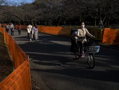 Orang-orang melewati jalan setapak di antara pagar yang ditempatkan untuk menutup bagian taman untuk mencegah pesta melihat bunga sakura (Hanami) di bawah pohon untuk pencegahan keamanan terhadap COVID-19 di salah satu tempat Hanami paling populer di Tokyo (13/3/2021).  (AP Photo/Kiichiro Sato)