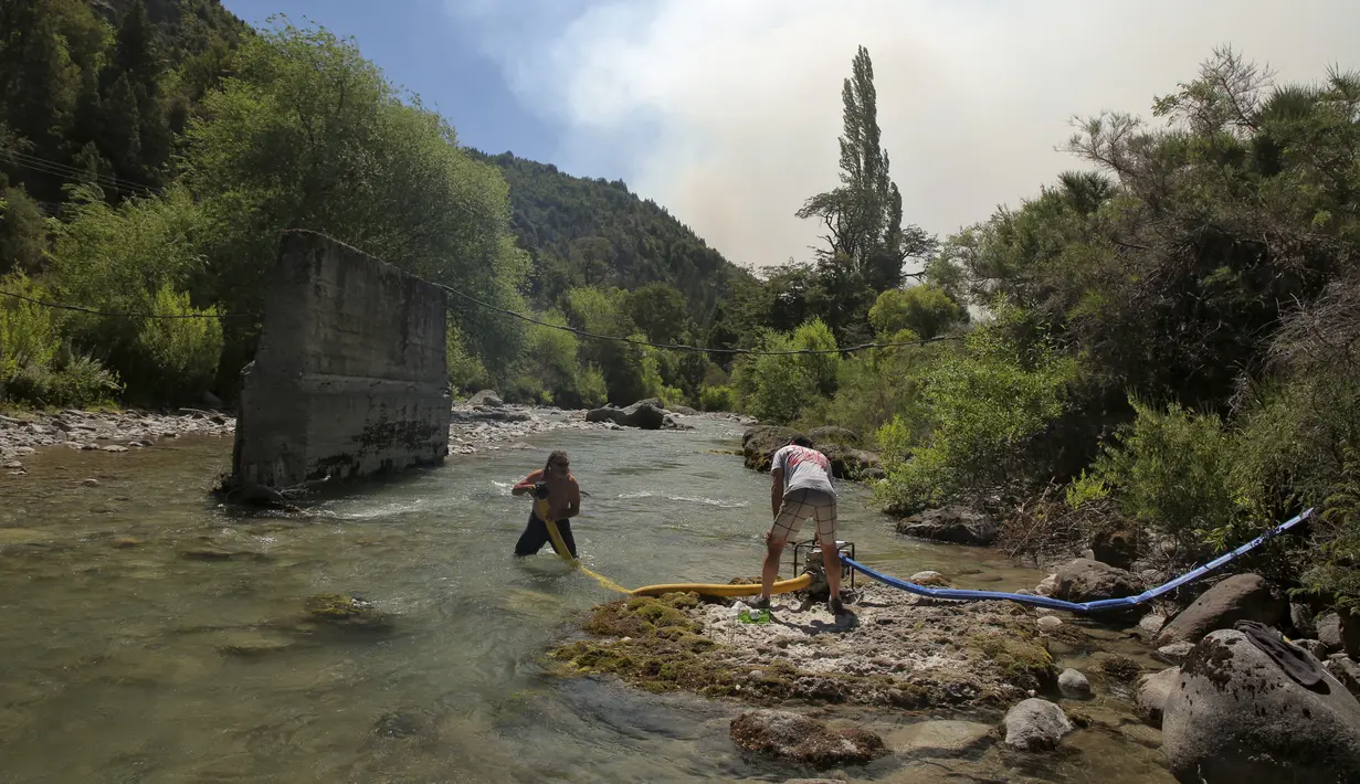 Orang-orang memompa air dari sungai untuk memadamkan kebakaran hutan besar di dekat Paraje Villegas, Provinsi Rio Negro, 70 km selatan Bariloche, Argentina (24/12/2021). Kebakaran berkobar di dataran tinggi, kawasan hutan berpenduduk sedikit. (AFP/ Francisco Ramos Meija)