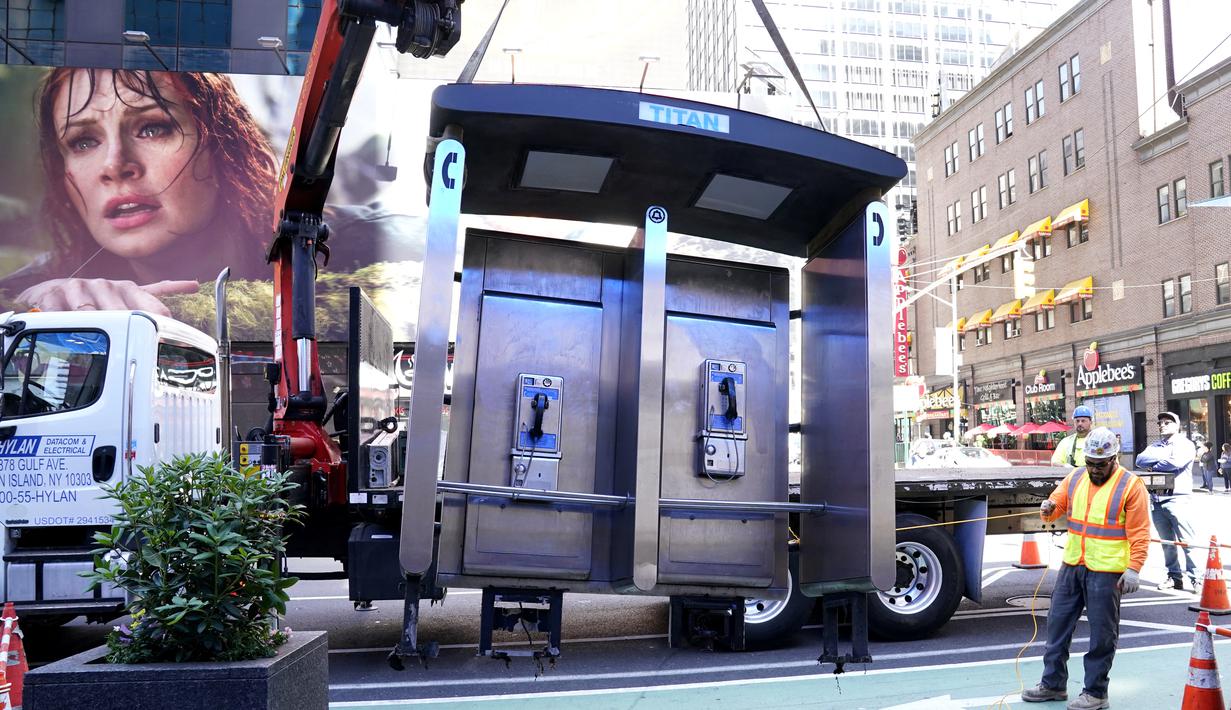 Para pekerja memindahkan bilik telepon umum terakhir NYC di dekat Seventh Avenue dan 50th Street di Midtown Manhattan, New York City, Amerika Serikat (AS) pada 23 Mei 2022. Menandai berakhirnya sebuah era, Kota New York pada hari Senin menghapus bilik telepon umum yang telah menjadi "korban" karena kemunculan teknologi informasi seperti Wi-Fi gratis dan telepon seluler. (TIMOTHY A. CLARY / AFP)