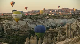 Balon udara membawa wisatawan naik ke langit saat matahari terbit di Kapadokia, Turki, Selasa (7/8). Cerobong Peri Kapadokia adalah lansekap batu vulkanik berbentuk kerucut yang menjulang tinggi ke langit. (AP Photo/Emrah Gurel)
