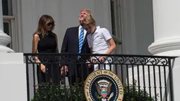 Presiden AS Donald Trump bersama Ibu Negara, Melania Trump dan putra mereka, Barron melihat gerhana matahari dari balkon Gedung Putih di Washington, Senin (21/8). Trump terlihat menyaksikan fenonema langka itu tanpa kacamata pelindung. (NICHOLAS KAMM/AFP)