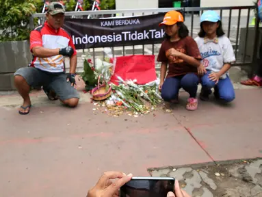 Warga berfoto di dekat poster #Indonesiatidaktakut yang dipasang di depan Menara Cakrawala, Jakarta, Sabtu (16/1). Lokasi teror di kawasan Sarinah Thamrin terus didatangi warga untuk mengabadikan diri atau foto selfie. (Liputan6.com/Faizal Fanani)