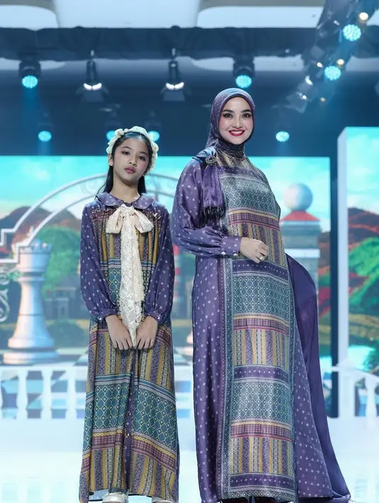 Ririn Ekawati tampil serasi bersama putrinya dalam balutan busana bernuansa ungu yang terasa lembut sekaligus berkarakter. Ririn mengenakan long dress bermotif geometris dengan dominasi warna ungu tua, biru, dan sentuhan emas. Sang anak tampil dalam dress bermotif serupa, dirancang lebih playful lewat sentuhan pita renda besar berwarna krem di bagian leher yang langsung menjadi focal point. [Dok/Shi by Shireen & Zaskia Sungkar].