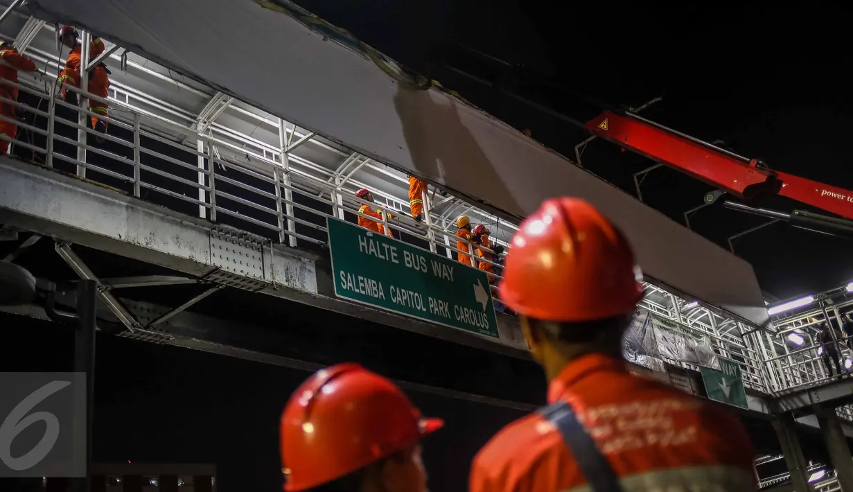 Petugas dari Dinas Pemadam Kebakaran berusaha melepaskan papan reklame yang terpasang di dinding JPO kawasan Salemba, Jakarta, Rabu (26/10) malam. Pembongkaran dilakukan lantaran  papan reklame itu diketahui tidak berizin. (Liputan6.com/Faizal Fanani)