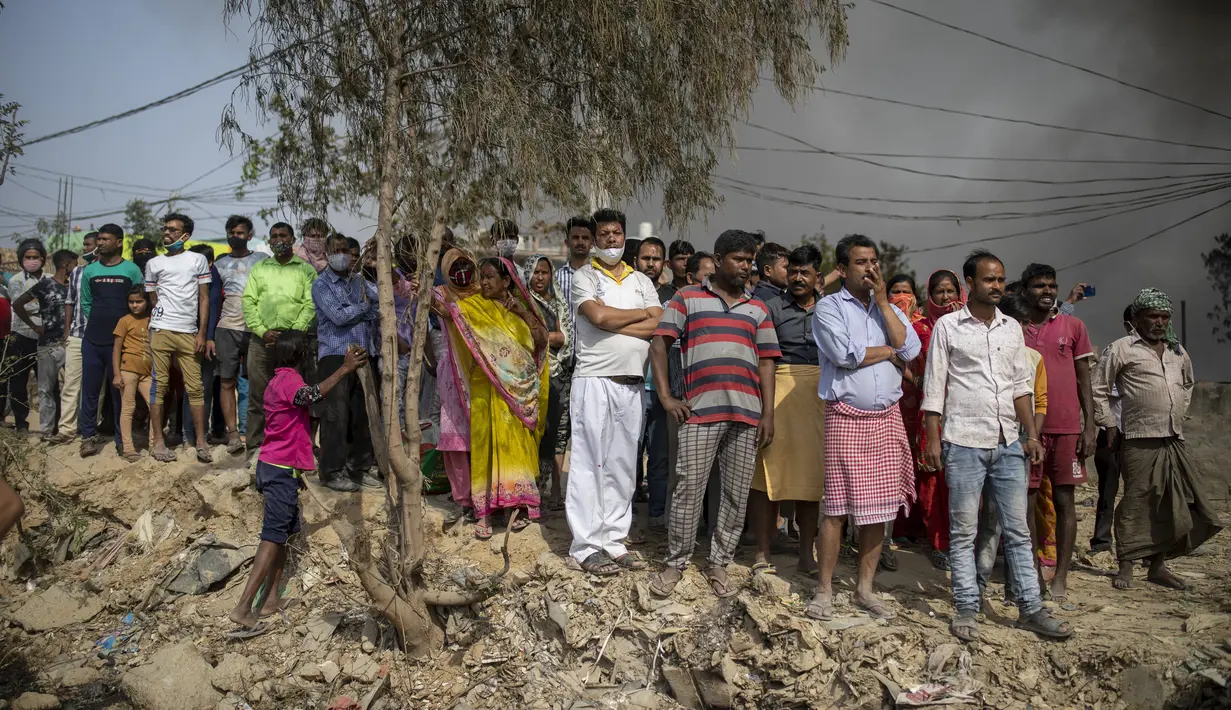Orang-orang menyaksikan kebakaran di daerah kumuh di Noida, pinggiran kota New Delhi, India, Minggu (11/4/2021). Dua anak tewas dan lebih dari 150 gubuk kumuh yang sebagian besar dihuni oleh para pemulung dalam kebakaran pada Minggu sore. (AP Photo/Altaf Qadri)