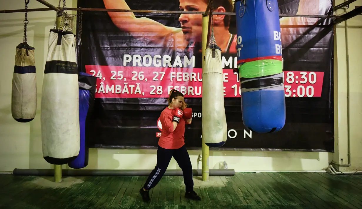Seorang petinju wanita muda meninju tas tinju sebagai spanduk yang menunjukkan juara kotak Steluta Duta terlihat di latar belakang, selama sesi pelatihan di Buzau, Rumania (17/1/2020). (AFP/Daniel Mihailescu)