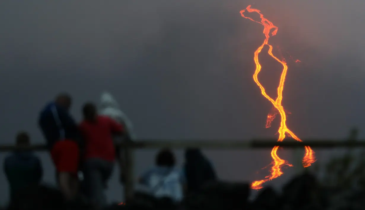 Warga melihat guguran lava pijar yang keluar dari gunung api Piton de la Fournaise atau Peak of the Furnace di Pulau Reunion, Samudera Hindia, Prancis, Selasa (13/8/2019). Letusan Piton de la Fournaise berlanjut hingga hari ketiga. (Richard BOUHET/AFP)