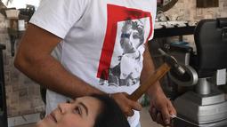 Dalam gambar pada 8 April 2021, tukang cukur Pakistan Ali Abbas menggunakan palu dan pisau daging untuk memotong rambut pelanggan di tokonya di Lahore. Berharap membuktikan kemampuannya dalam persaingan, Ali Abbas mengandalkan berbagai alat yang tidak biasa untuk melatih keahliannya. (Arif ALI/AFP)