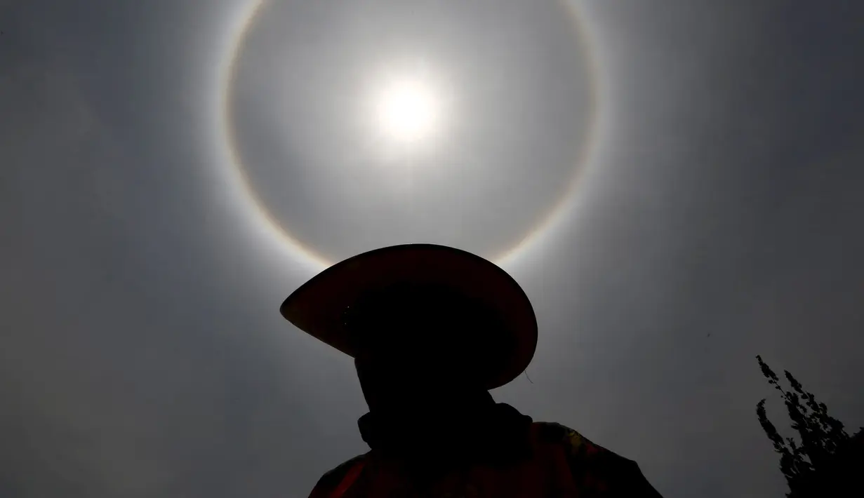 Seorang pria mengunakan topi saat berada di bawah 'Halo Matahari' di Mexico City, Kamis (21/5/2015). Menurut ahli meteorologi, fenomena cuaca menciptakan pelangi mengelilingi matahari dan dibentuk oleh refleksi dari kristal es. (REUTERS/Edgard Garrido)