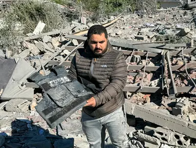Seorang pria memegang rompi rusak bertuliskan “Press” di tengah puing-puing lokasi serangan udara Israel yang menargetkan area di mana sejumlah wartawan berada di desa Hasbaya, Lebanon selatan, pada Jumat 25 Oktober 2024. (Ali Hankir/AFP)