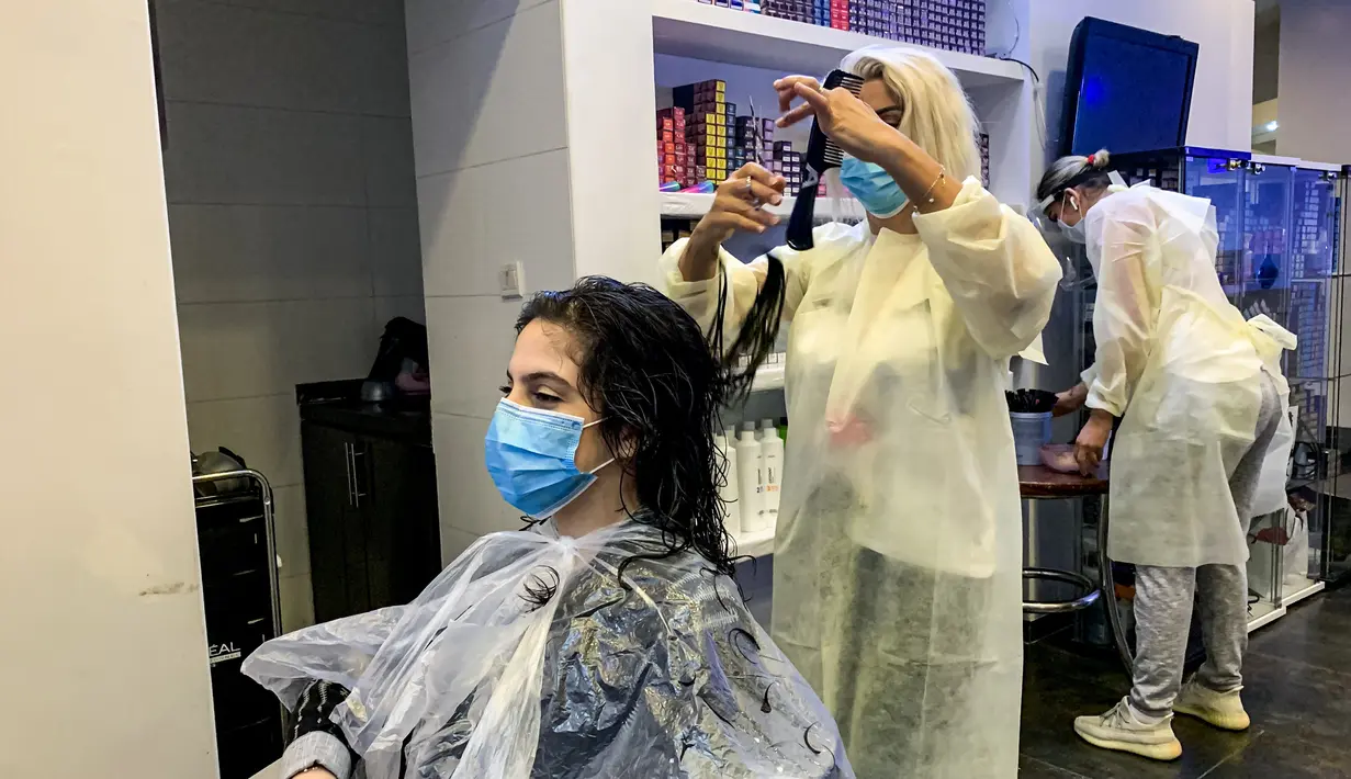Seorang penata rambut mengenakan masker memotong rambut pelanggannya di sebuah pusat kecantikan wanita di Riyadh, Arab Saudi (21/6/2020). Pemerintah Arab Saudi mulai membuka kembali kegiatan perekonomian setelah melonggarkan lockdown Covid-19. (AFP Photo/Rania Sanjar)