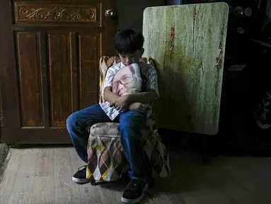 Kian Navales berpose di rumahnya sambil memegang bantal dengan foto mendiang ayahnya, Arthur, yang meninggal karena virus corona di kota Quezon, Filipina pada 6 Juli 2021. Navales, yang juga terkena COVID-19, rindu pergi makan mie bersama ayahnya.  (AP Photo/Aaron Favila)