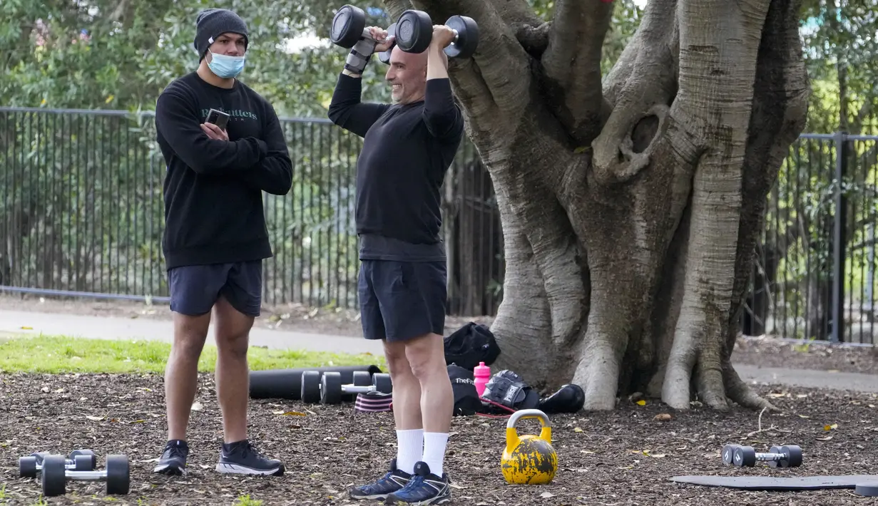 Seorang trainer menyaksikan anggota fitness berolahraga di sebuah taman di pinggiran timur Sydney, pada 14 September 2021. Pelatih pribadi telah mengubah taman kawasan tepi laut di Rushcutters Bay menjadi gym luar ruangan untuk menyiasati pembatasan lockdown karena pandemi covid-19. (AP/Mark Baker)