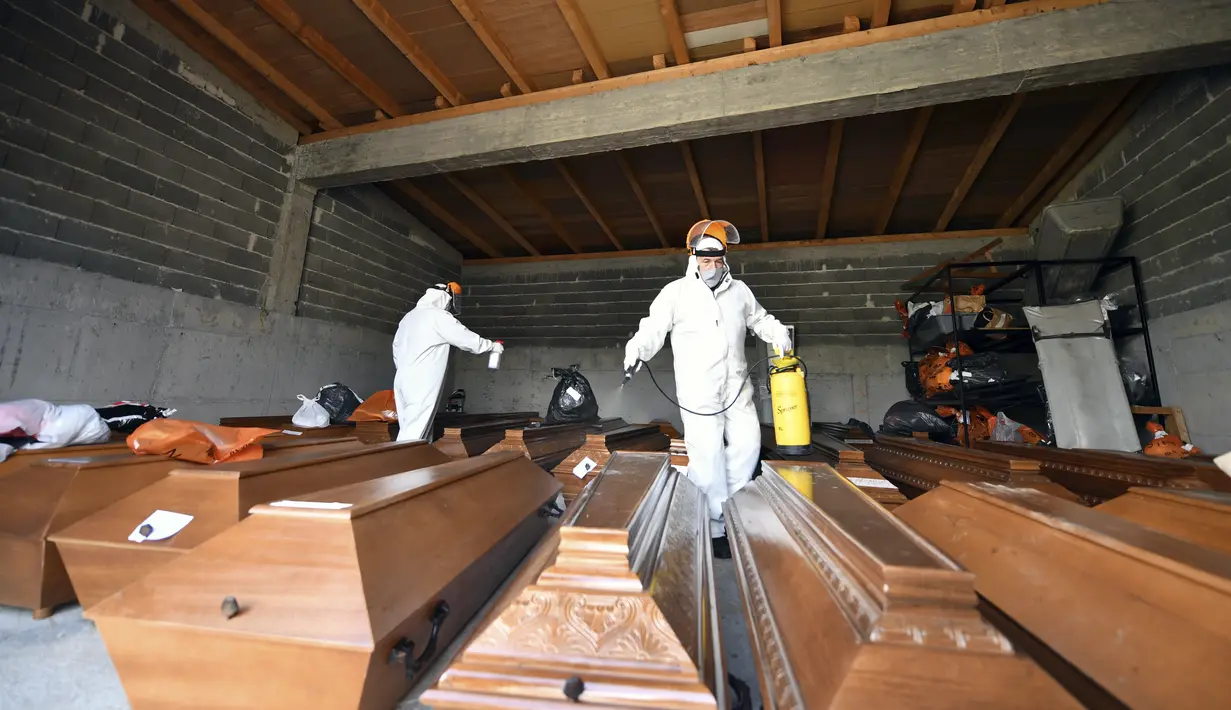 Pekerja menyemprotkan disinfektan di atas peti mati yang diletakkan di lantai kamar mayat di pemakaman Sarajevo Bare, Bosnia, Jumat (19/3/2021). Rumah sakit dan kamar mayat di Sarajevo kewalahan mengatasi meningkatnya infeksi dan lonjakan kematian yang disebabkan oleh virus corona. (AP Photo)