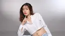 Tasya tampil menawan dengan balutan kemeja putih crop top dan celana jeans longgar. Dengan pose santai di lantai, ia memancarkan kebahagiaan dan kebanggaan atas kehamilan keduanya. Senyumnya yang lembut semakin menambah aura kehangatan dalam foto tersebut. (Liputan6.com/IG/@tasyarevina)