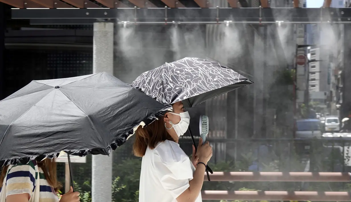 Seorang wanita mengenakan masker wajah untuk membantu melindungi dari penyebaran virus corona menggunakan kipas angin portabel di dekat titik kabut pendingin di sebuah jalan di Tokyo, Selasa (10/8/2021). (AP Photo/Eugene Hoshiko)