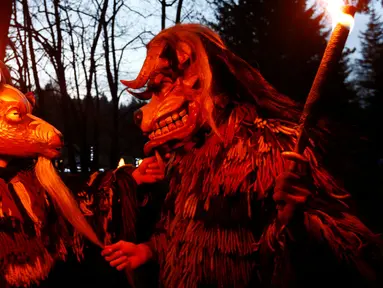 Peserta mengenakan kostum iblis membawa obor saat mengikuti parade tardisional Perchtenlauf di Osterseeon dekat Munchen, Jerman (17/12). Dalam sejarahnya, kata Perchten berarti topeng perempuan yang menyimbolkan dewi kuno. (Reuters/Michaela Rehle)
