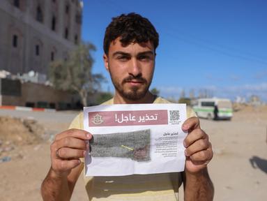 Seorang pria Palestina menunjukkan salah satu selebaran yang disebarkan oleh tentara Israel di Beit Hanun, Jalur Gaza utara pada 19 Maret 2025. (BASHAR TALEB/AFP)