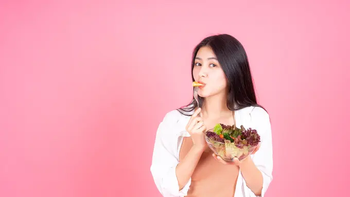Seorang perempuan berbaju pink sedang makan semangkuk salad (Foto Dok: Freepik/jcomp)
