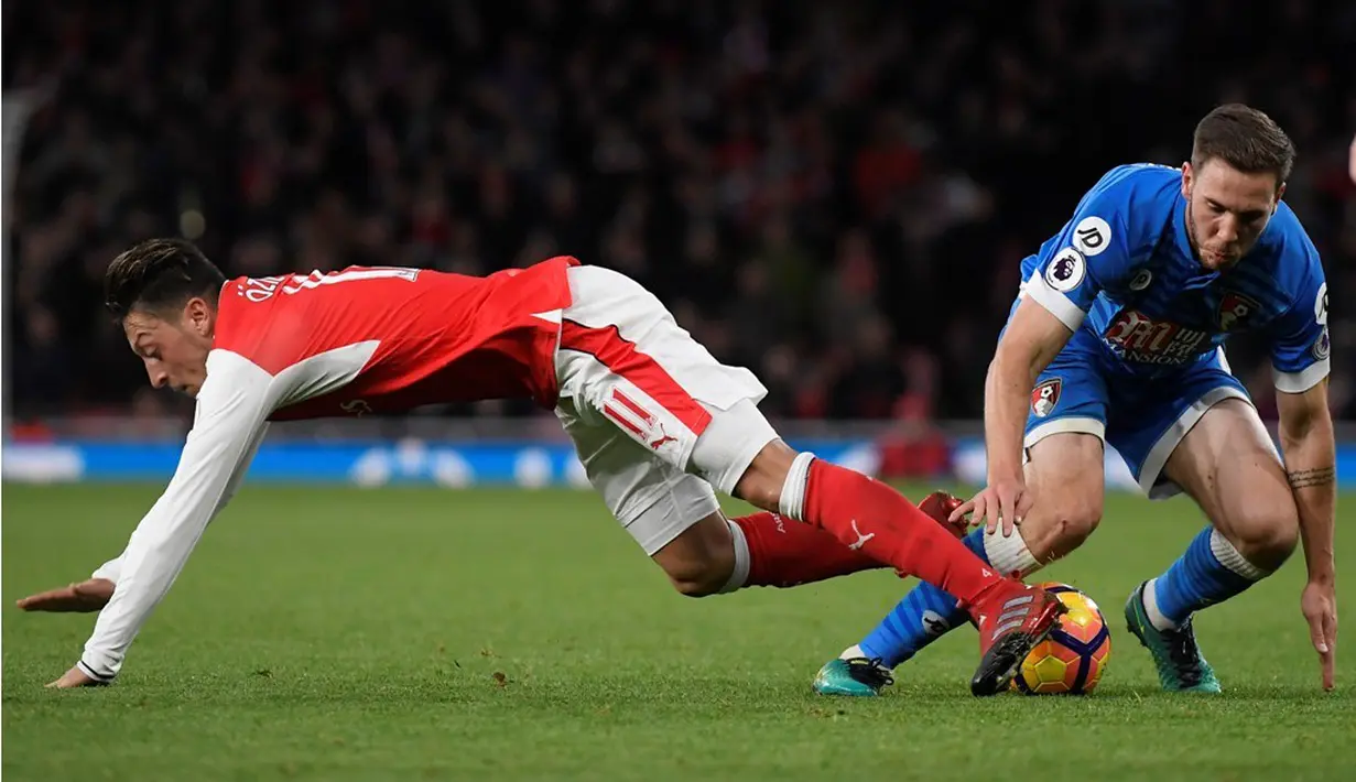 Pemain Arsenal, Mesut Ozil, terjatuh saat berebut bola dengan pemain AFC Bournemouth, Dan Gosling, dalam laga pekan ke-13 Premier League 2016-2017 di Stadion Emirates, Minggu (27/11/2016). (Reuters/Toby Melville)