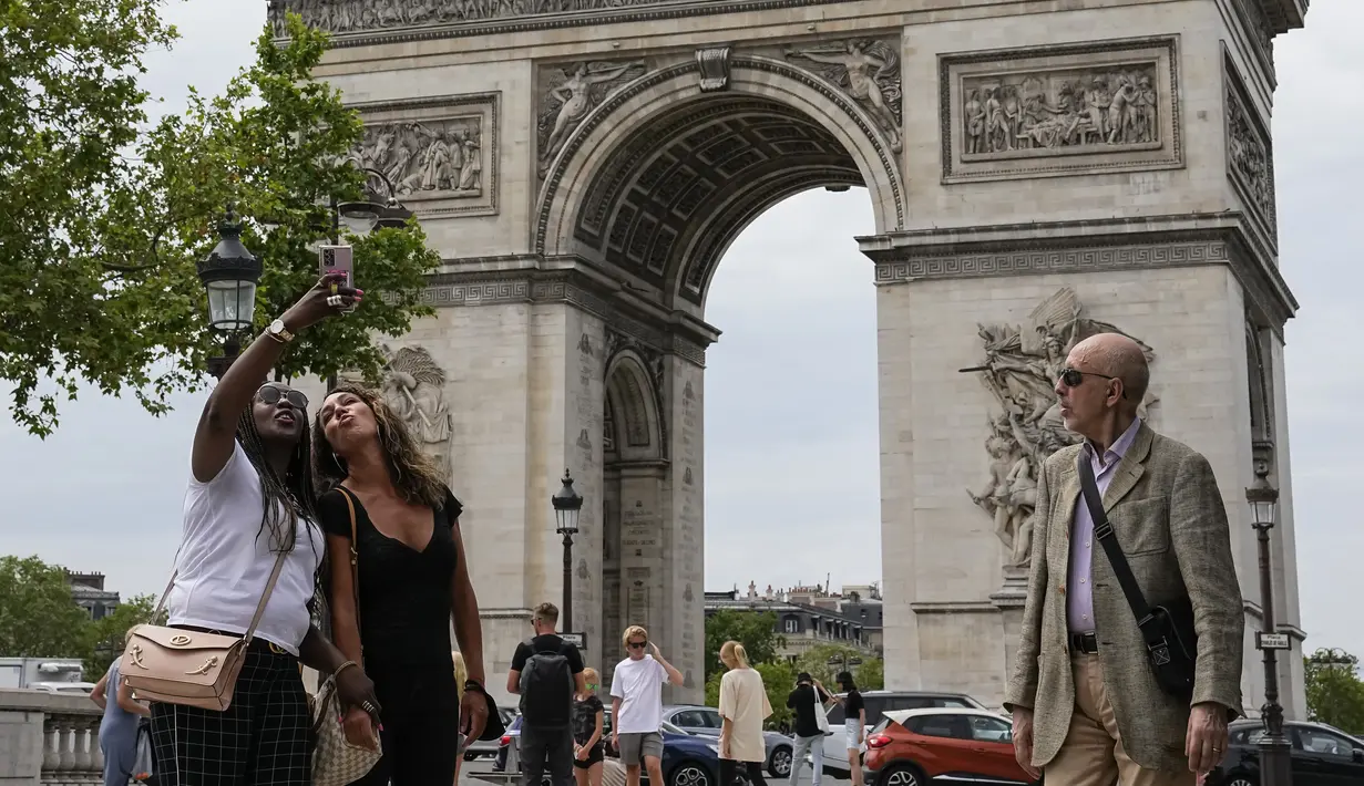 Orang-orang berswafoto dengan latar belakang Arc de Triomphe di jalan Champs Elysees, Paris, Kamis (17/6/2021). Prancis mengumumkan melonggarkan aturan pembatasan COVID-19, mencabut aturan penggunaan masker di luar ruangan dan menghentikan jam malam mulai pekan ini. (AP Photo/Michel Euler)
