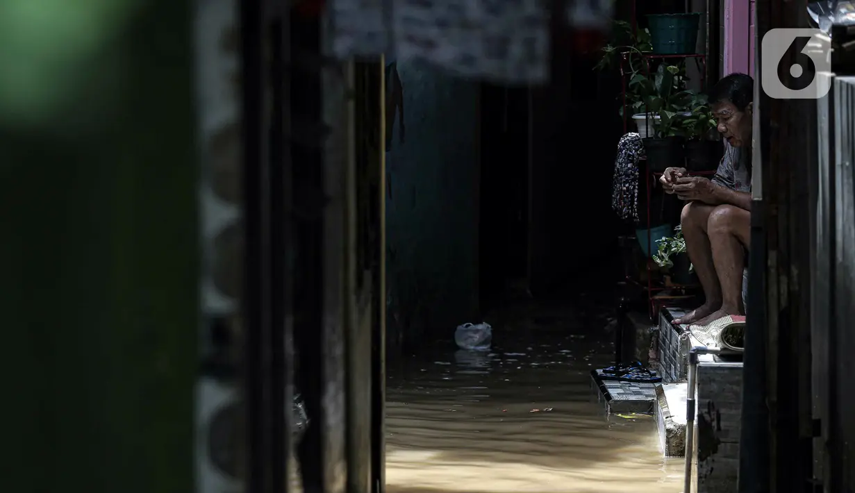 Warga bersantai saat banjir di kawasan Kampung Melayu, Jakarta, Senin (8/11/2021). Banjir akibat luapan Kali Ciliwung tersebut merendam pemukiman setinggi 60 cm sejak 7 November 2021 sore. (Liputan6.com/Faizal Fanani)