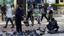 Orang-orang yang memakai masker untuk membantu melindungi dari penyebaran virus corona COVID-19 memberi makan burung merpati di sebuah jalan di Goyang, Korea Selatan, Rabu (11/11/2020). (AP Photo/Ahn Young-joon)