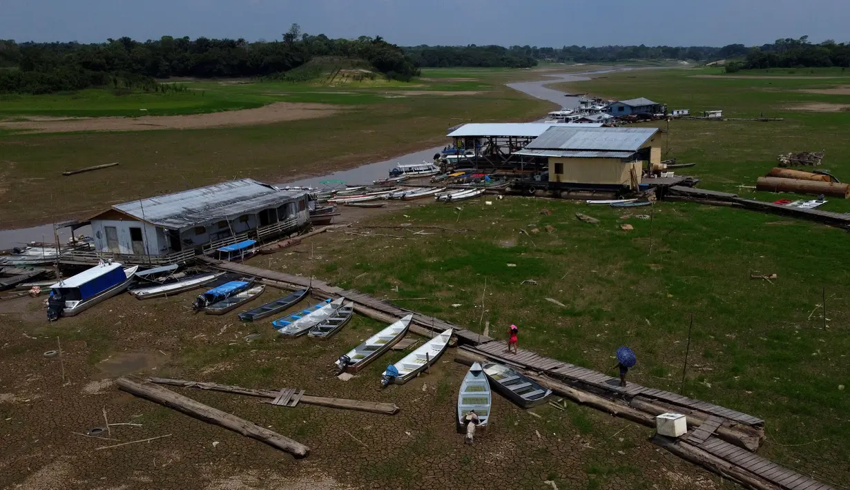 Warga berjalan di samping rumah dan perahu di hamparan Sungai Solimoes yang kering di daerah pedesaan negara bagian Amazonas, Brasil, Sabtu, 21 Oktober 2023. (AP Photo/Edmar Barros)