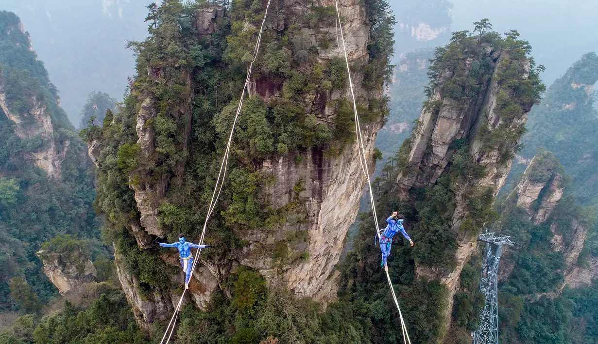 Dua kontestan berpakaian karakter Avatar berpacu sepanjang slackline di Pegunungan Huangshizhai di Zhangjiajie, Hunan, China, Minggu (23/12). Aksi tersebut dilakukan saat mengikuti slackline internasional.  (STR/AFP)