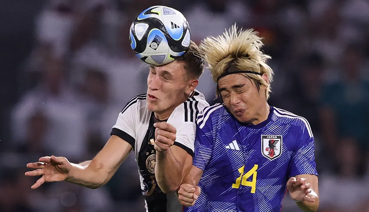 Bek Jerman #20 Robin Gosens (Kiri) dan gelandang Jepang #14 Junya Ito keduanya melompat untuk menyundul bola pada laga uji coba internasional di Stadion Volkswagen Arena, Minggu (10/9/2023) dini hari WIB. (Photo by Ronny HARTMANN / AFP)