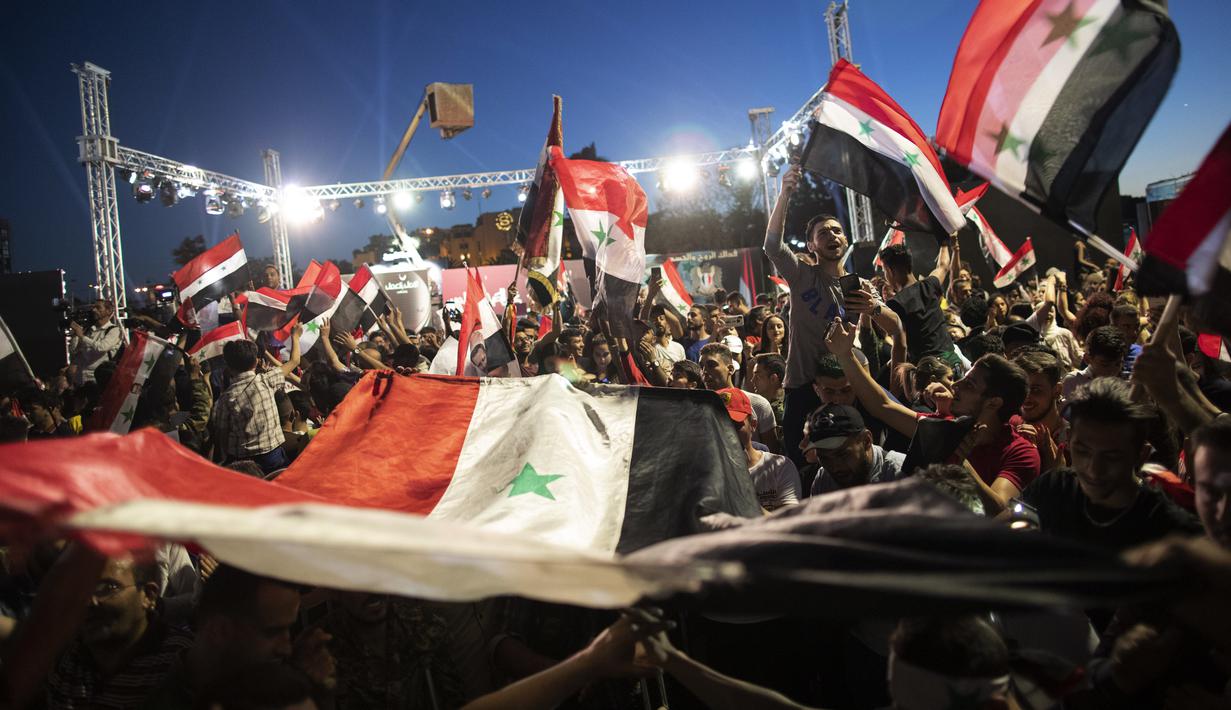 Pendukung mengibarkan bendera nasional dan foto Presiden Suriah Bashar Assad saat mereka merayakan kemenangannya di Omayyad Square, di Damaskus, Kamis (27/5/2021). Bashar al-Assad terpilih kembali untuk masa jabatan keempat sebagai presiden Suriah yang dilanda perang. (AP Photo/Hassan Ammar)