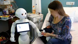 Robot humanoid bernama Pepper berdiri di samping seorang ibu dan bayinya yang baru lahir di rumah sakit AZ Damiaan di Ostend, Belgia (16/6). Robot dirancang atau dibuat untuk mengurus pasien yang datang ke rumah sakit ini. (REUTERS / Francois Lenoir)