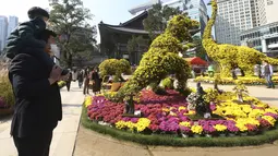 Seorang anak laki-laki dan ayahnya melihat Jam tangan dinosaurus yang terbuat dari bunga krisan selama festival Krisan di kuil Chogyesa di Seoul, Senin (19/10/2020). Korsel mulai menguji puluhan ribu karyawan rumah sakit dan panti jompo untuk mencegah wabah COVID-19. (AP Photo/Ahn Young-joon)