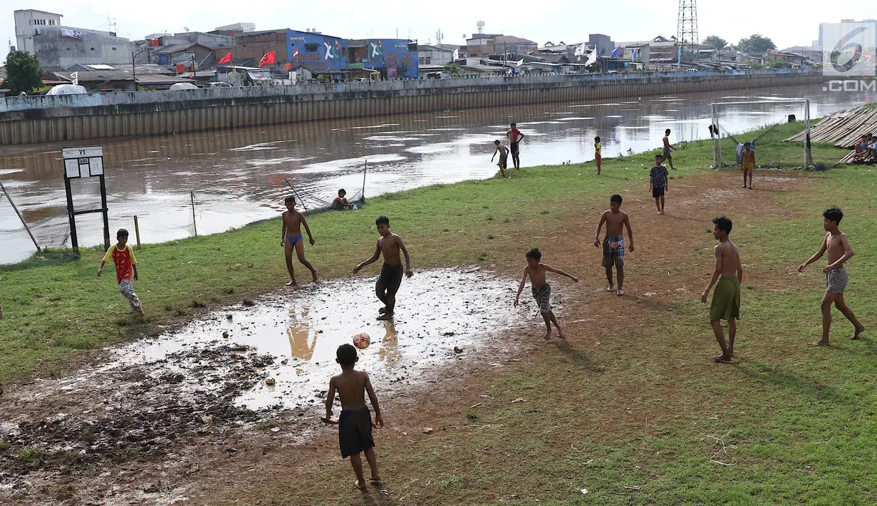 Anak-anak bermain sepak bola di bantaran Kanal Banjir Barat, Jakarta, Jumat (5/4). Tidak adanya lapangan menjadikan lokasi tersebut sebagai tempat bermain mereka, meskipun dalam kondisi seadanya. (Liputan6.com/Immanuel Antonius)